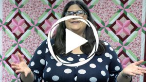 a woman in a polka dot shirt stands in front of a quilt